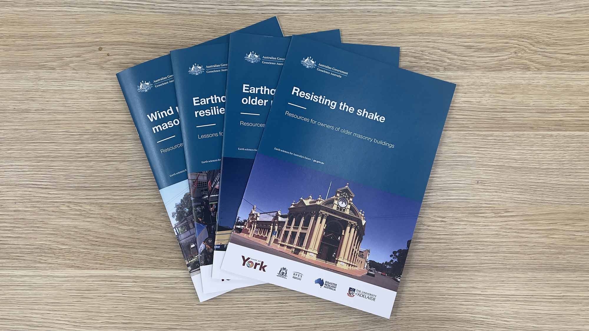 Four A4 booklets with dark teal branding arranged in a fan shape. The top booklet reads 'Resisting the shake - Resources for the owners of older masonry buildings'.