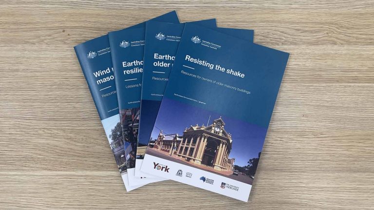 Four A4 booklets with dark teal branding arranged in a fan shape. The top booklet reads 'Resisting the shake - Resources for the owners of older masonry buildings'.