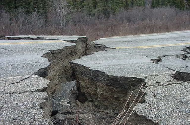 Damaged asphalt road with a large, deep crack running down the center.