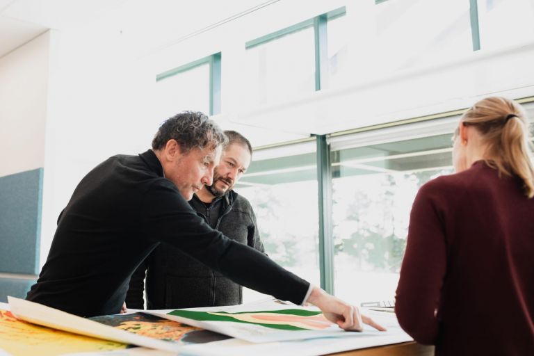 Three people stand at a table looking at cyclone tracking maps