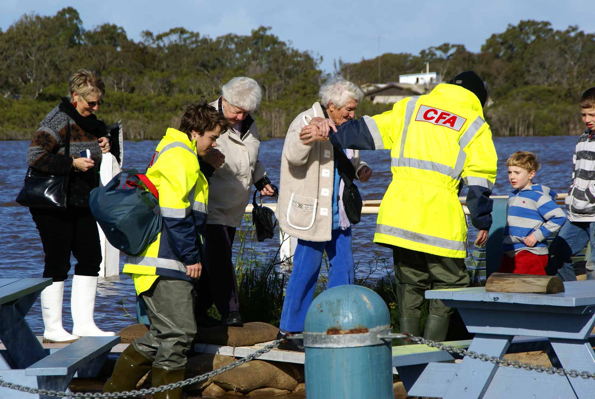 CFA image library shoes a CFA volunteer helping a man out of a boat after travelling over flood waters