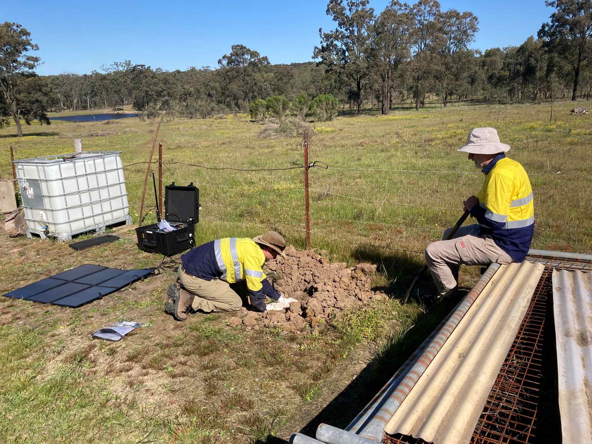 Two men in hi-vis clothing digging a hole to install earthquake monitoring equipment