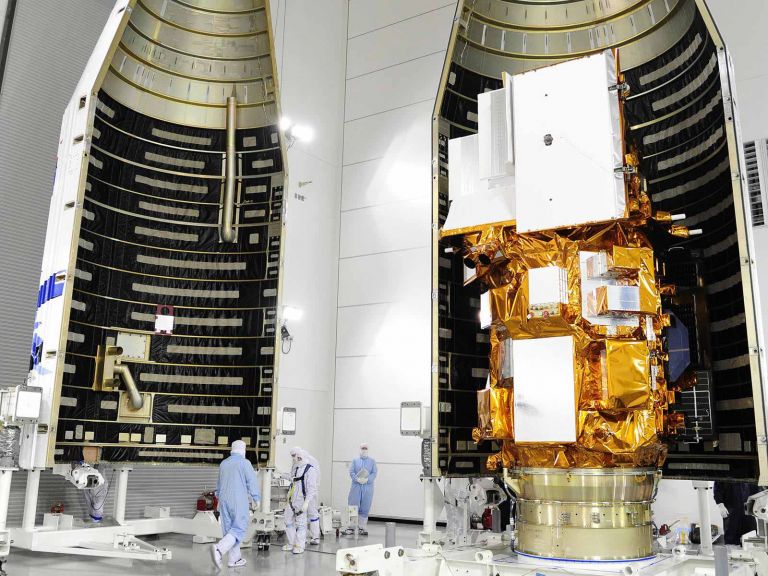 Satellite in construction in vast indoor space with technicians