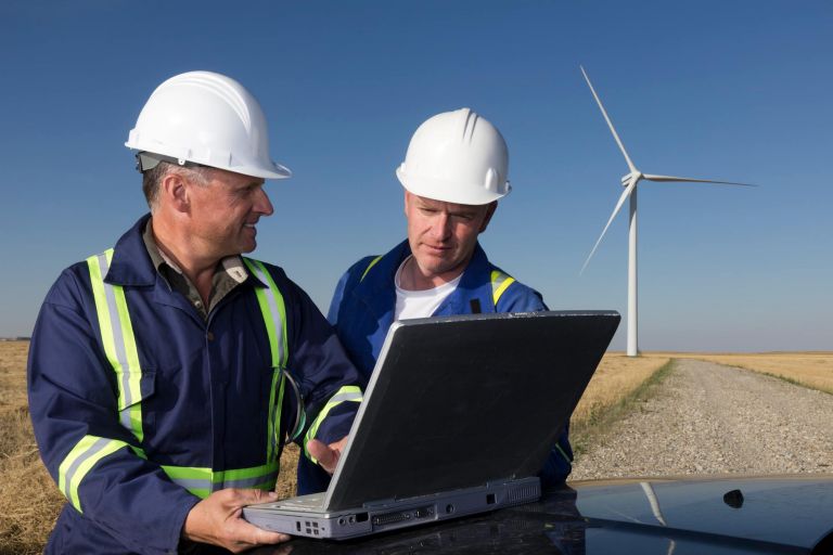 Two workers using a laptop computer in front of a wind turbine