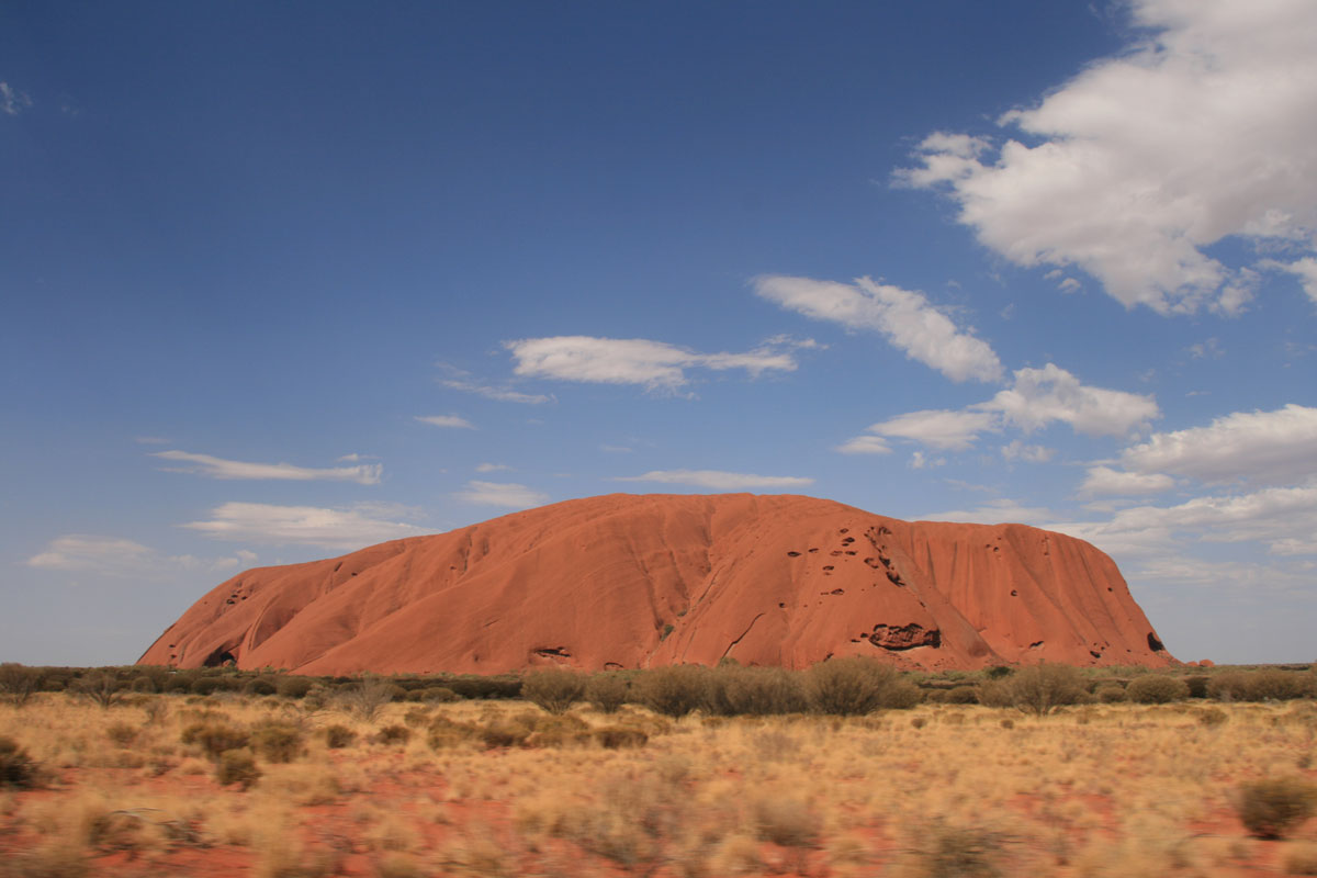 Large red rock in a dry landscape under a blue sky with clouds