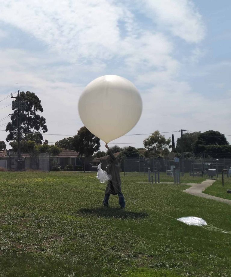 Man in yard releasing large weather ballon carrying scientific measurement equipment.